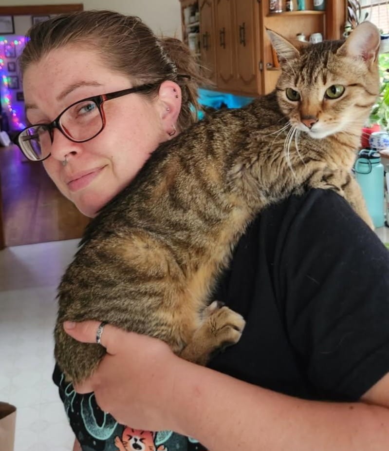 Kim holding a brown tabby cat on her shoulder.